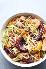 Stir-fry noodles with sea food in bowl on light grey table, top view