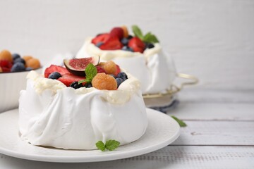Pavlova cake (meringue dessert) with whipped cream, fresh berries, fig and mint on white wooden table, closeup