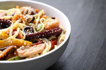 Stir-fry noodles with sea food in bowl on grey textured table, closeup. Space for text