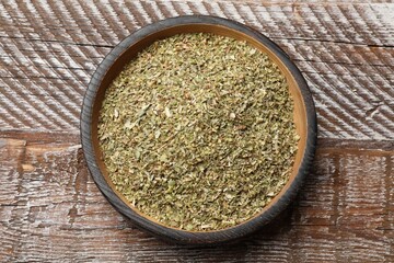 Dried oregano in bowl on wooden table, top view