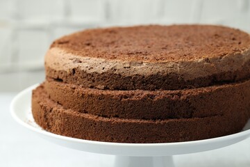 Cut chocolate sponge cake on stand against light background, closeup