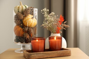 Burning candles and autumn decor on wooden table indoors, closeup