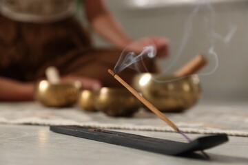 Incense stick smoldering in holder on floor indoors, selective focus