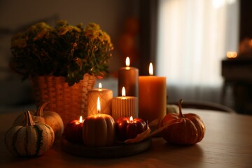Burning candles, pumpkins and flowers on wooden table indoors. Space for text