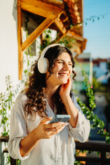 Young caucasian woman listening to music or audio book on her balcony
