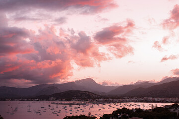 Port de Pollença mit Segelbooten und dem Tramuntana Gebirge im Hintergrung und rot angestrahlen Wolken nach Sonnenuntergang.