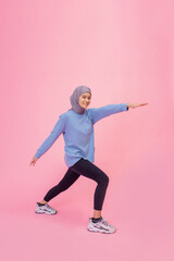 A woman in vibrant sportswear gracefully stretches against a bright pink background