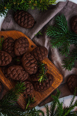 Christmas chocolate pine cone cookies laid on a wooden board, decorated with fir branches. New Year's Chocolate Cookies. Top view close-up