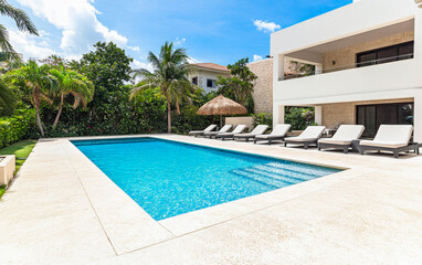 Fototapeta premium Luxurious outdoor swimming pool surrounded by palm trees and lounge chairs in a sunny tropical setting