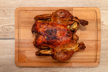 A whole roasted chicken lying on a wooden board on the table.