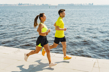 Two Runners in Bright Sportswear Jogging Along a Waterfront Path on a Sunny Day in an Urban Setting