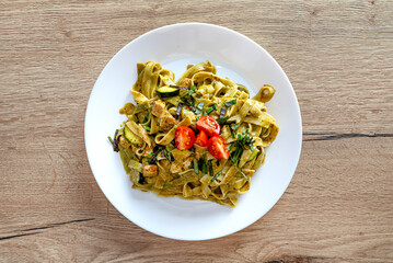 Pesto with tagliatelle with chicken and cherry tomatoes lying on a plate.