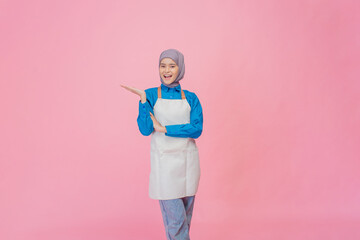 A smiling female chef in an apron, holding a rolling pin against a pink backdrop.