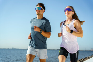 Two Joggers Run Along a Waterfront Path on a Sunny Day, Enjoying Their Fitness Routine Together...