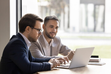 Two handsome young business colleagues men using laptop at workplace together for Internet...