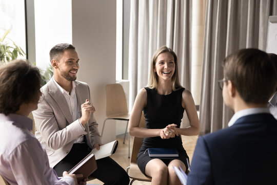 Happy cheerful coworkers sitting in circle in office, brainstorming on project ideas, talking, discussing startup, laughing, listening to group leader. Group therapy meeting
