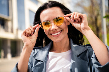 Photo of grinning pretty lady dressed grey jacket dark eyewear enjoying sunshine outdoors town street