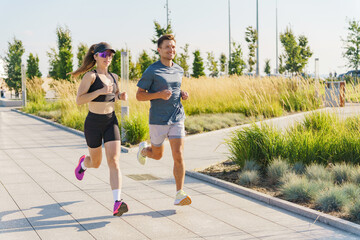 Two Individuals Enjoy Jogging Together on a Sunny Day Along a Scenic Park Pathway Surrounded by Greenery and Urban Design