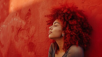 A woman with red hair is leaning against a red wall