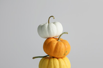 A stack of three decorative pumpkins in white, orange, and yellow against a neutral background