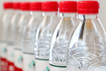 Close up of line of clear plastic bottles of water with red caps. Hydration, drinking water, healthy lifestyle concept. Selective focus.