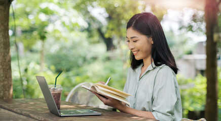 Fototapeta premium Asian business woman working outside creative notes ideas innovation, using laptop computer portable device wireless remote technology, digital online freelance worker outdoor sitting at cafe sunlight
