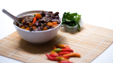 Sup daging kacang merah, clear soup with beef slices, red bean and vegetables. Served in bowl on wooden background. Selected focus.