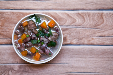 Sup daging kacang merah, clear soup with beef slices, red bean and vegetables. Served in bowl on wooden background. Selected focus.
