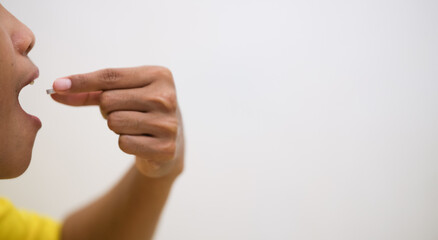 Close-up of a teenage girl taking a white pill, focusing on her lips and the capsule with a white background.