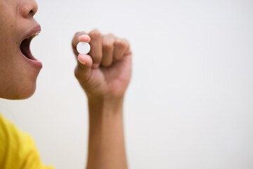 Close-up of a teenage girl taking a white pill, focusing on her lips and the capsule with a blurred background.