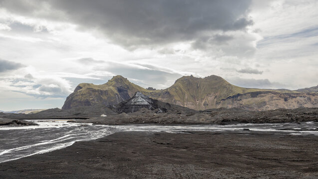 Ash covered Kalta Ice Cave and sorrounding mountains with glacial river, Iceland