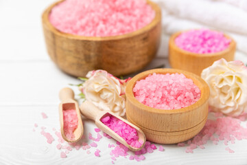 Sea salt for bath with aroma and rose flowers on textured wooden background. Pink sea salt. Spa treatments. Natural salt with herbs and essential oils. skincare concept. Meso for text. Copy space