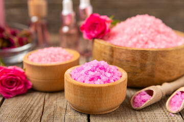 Sea salt for bath with aroma and rose flowers on textured wooden background. Pink sea salt. Spa treatments. Natural salt with herbs and essential oils. skincare concept. Meso for text. Copy space