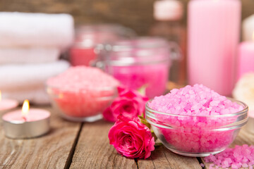 Sea salt for bath with aroma and rose flowers on textured wooden background. Pink sea salt. Spa treatments. Natural salt with herbs and essential oils. skincare concept. Meso for text. Copy space