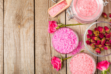Sea salt for bath with aroma and rose flowers on textured wooden background. Pink sea salt. Spa treatments. Natural salt with herbs and essential oils. skincare concept. Meso for text. Copy space