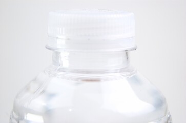 Close-up image of the top of a plastic bottle filled with water and its lid on a white background
