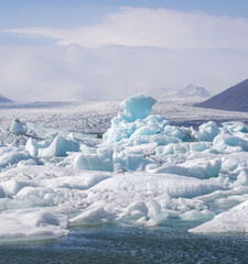 blue iceberg emerging from icy J&ouml;kuls&aacute;rl&oacute;n lagoon with Brei&eth;amerkurj&ouml;kull glacier in the background, Icleand