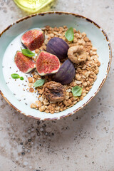 Green bowl with greek yogurt, granola, fresh and dried fig fruits, vertical shot on a beige granite background, middle closeup