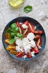 Tomato salad with ricotta and basil in a dark-blue bowl, vertical shot on a light-brown granite background, elevated view