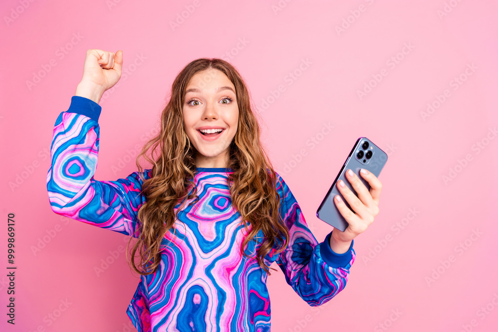 Wall mural Photo of pretty young woman hold phone raise fist wear pullover isolated on pink color background