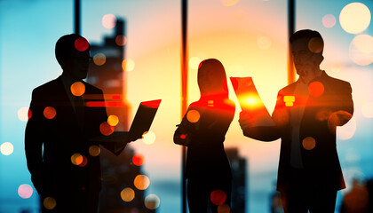Silhouette of businesspeople working together with laptop and documents against sunset background.
