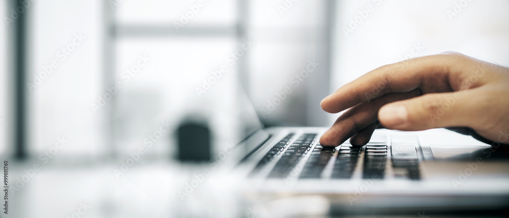 Poster Closeup of a hand typing on a laptop keyboard in an office environment with a blurred background.