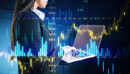 Businesswoman analyzing forex trading data on laptop with holographic financial graphs in blue digital background.