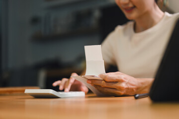Person using calculator while holding bills reviewing financial documents related to taxes and mortgage. The scene conveys a sense of focus and diligence in managing personal finances.