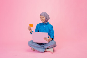 Happy girl with laptop and cards sitting on pink background, showcasing digital learning.