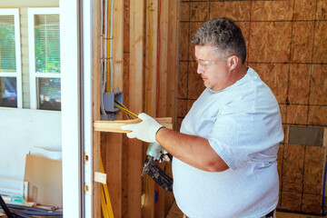 An carpenter uses pneumatic nail gun to install new front door in house