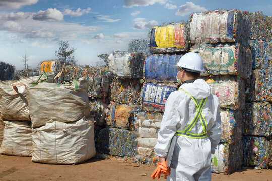Foreman in a protective suite and face mask inspecting separation of waste at a recycling centre, Thailand