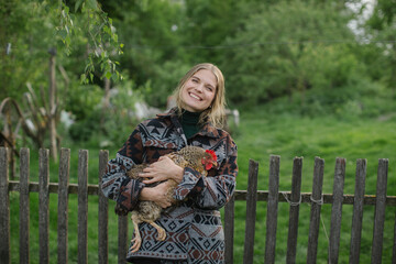 A young smiling woman holds a chicken in her hands while standing in a farm yard in the countryside. © dsheremeta