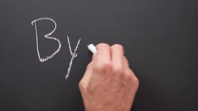 A hand writes the word bye with white chalk on a black board