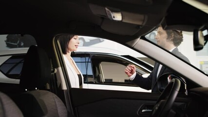 In a modern car dealership, the buyer and seller complete the car purchase with a handshake and an exchange of keys. Satisfaction from a successful purchase and the joy of owning a new car.